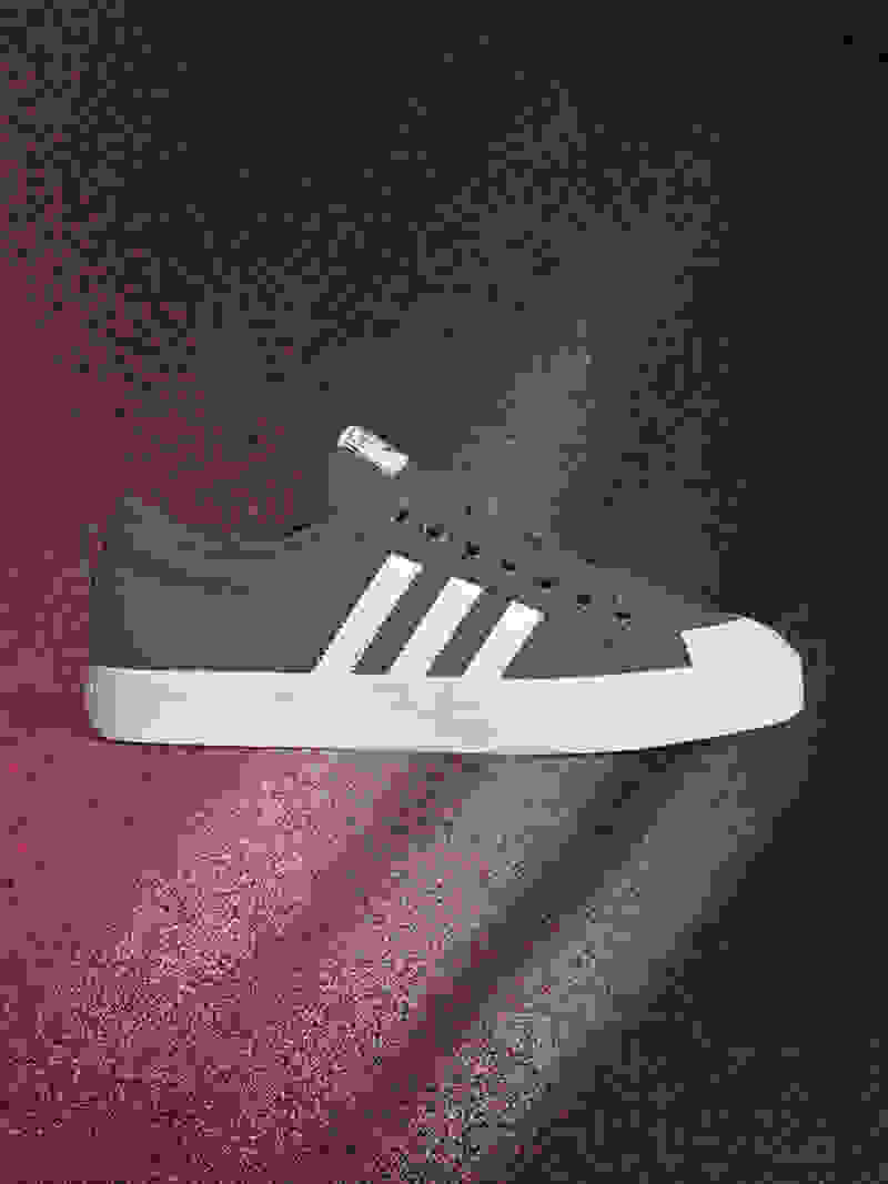 A gray and white sneaker is displayed against a dark, textured background with a reddish-pink gradient.