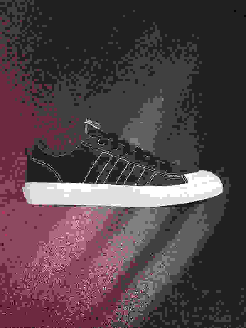 A black and white sneaker with a textured sole is displayed against a dark, moody background with a hint of red lighting.