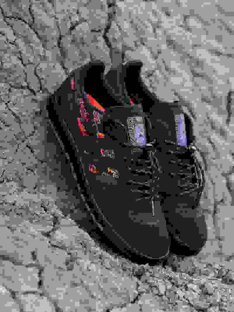 A pair of black and orange hiking shoes rests on a cracked, rocky surface against a gray, textured background.