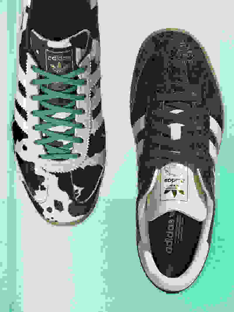 Een paar adidas sneakers met een zwart-wit patroon en groene veters, rustend op een mintgroene achtergrond.