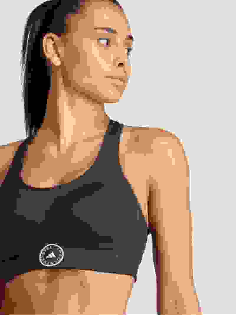 Een jonge vrouw die een zwarte sportbeha draagt, staat tegen een effen witte achtergrond, haar expressie gefocust en vastberaden.