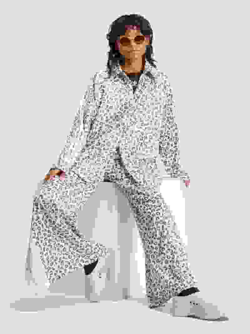 Iemand die een outfit met een witte en zwarte luipaardprint draagt, inclusief een jack en broek, prijkt op een witte achtergrond.