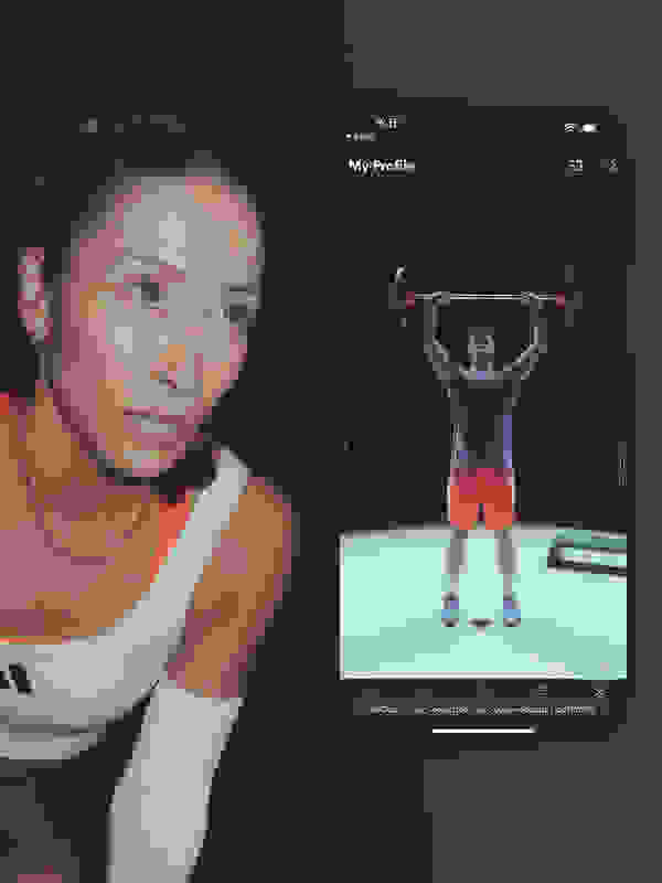 The image shows a woman with a serious expression on her face in the foreground, while in the background, there is a person lifting weights on a mobile device screen.
