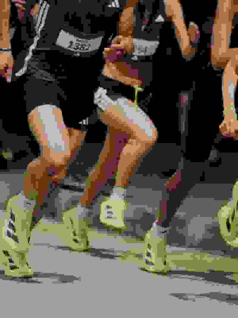 The image shows a person's lower body wearing black athletic shorts and colorful running shoes, standing on a tiled floor.