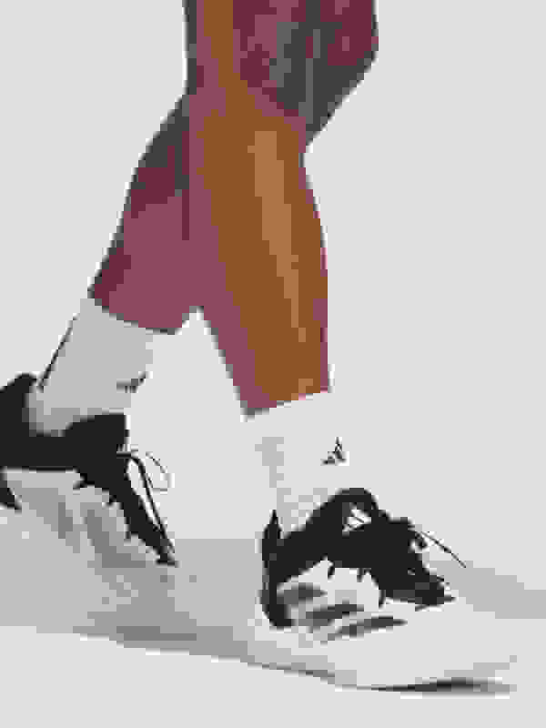 The image shows a person's lower body wearing white socks and black and white athletic shoes, standing on a plain white background.