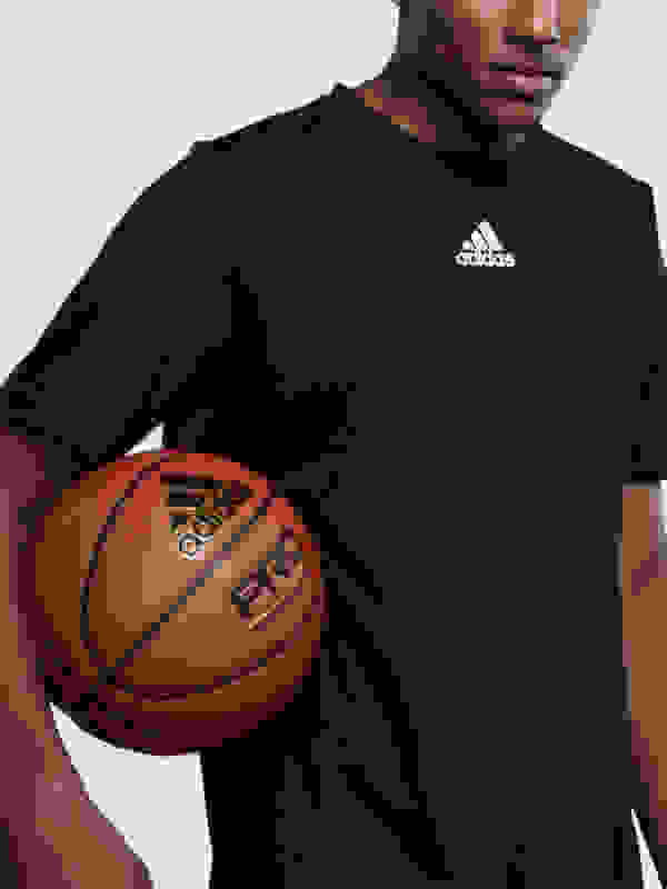 A person wearing a black Adidas shirt is holding a basketball in the foreground.