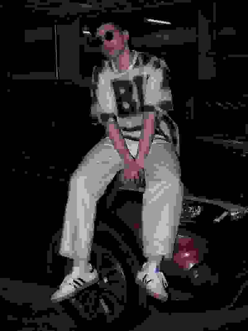 A person wearing a white jersey with the number "81" is sitting on a car tire in a dimly lit garage or warehouse setting.