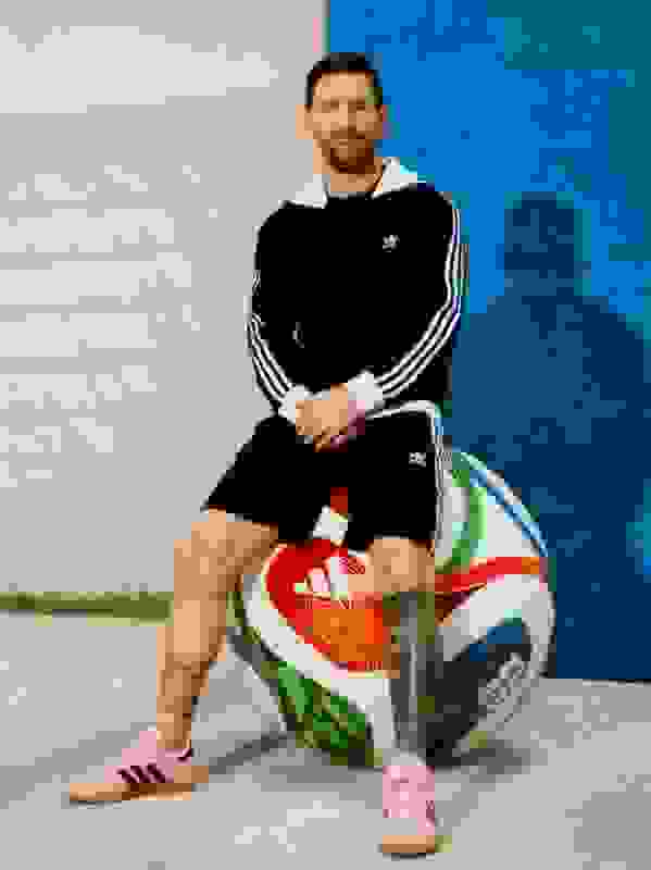A man in a black and white athletic outfit sits on a large, colorful inflatable ball against a bright blue background.