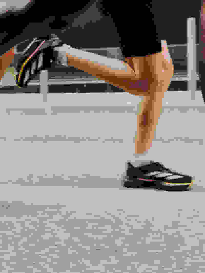 The image shows a person's lower body wearing black athletic shorts and colorful running shoes, standing on a tiled floor.