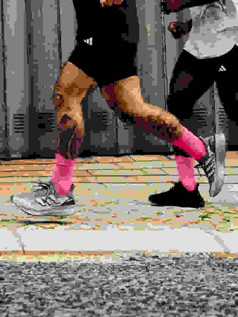 A group of people wearing athletic gear and running on a paved surface in front of a corrugated metal wall.