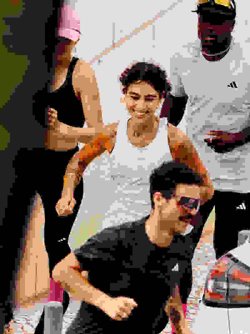 Aralarında siyah atletli bir kadın, beyaz bir tişörtlü bir erkek ve siyah bir tişörtlü başka bir erkeğin de bulunduğu bir grup genç, kentsel bir ortamda arka planda bir arabayla birlikte yürüyor.