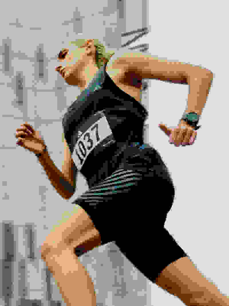 Spor giyim ürünleri giyen bir kadın, arka planda görünen yüksek binalarla kentsel bir ortamda koşuyor.