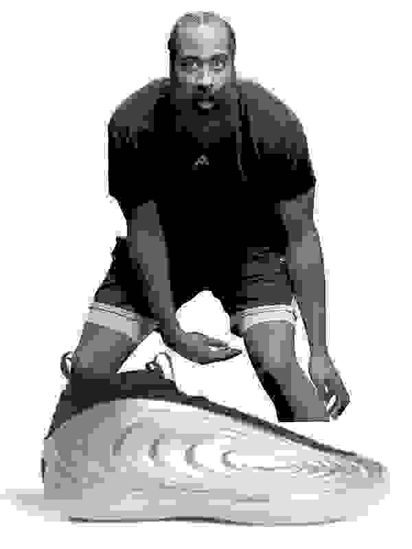 A muscular man with a thick beard is crouched down, intently focused on a spinning disc on the floor in front of him.