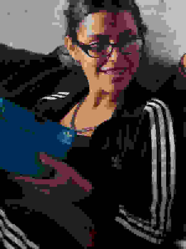 One person sitting against a wall holding a blue adidas shoe box. 