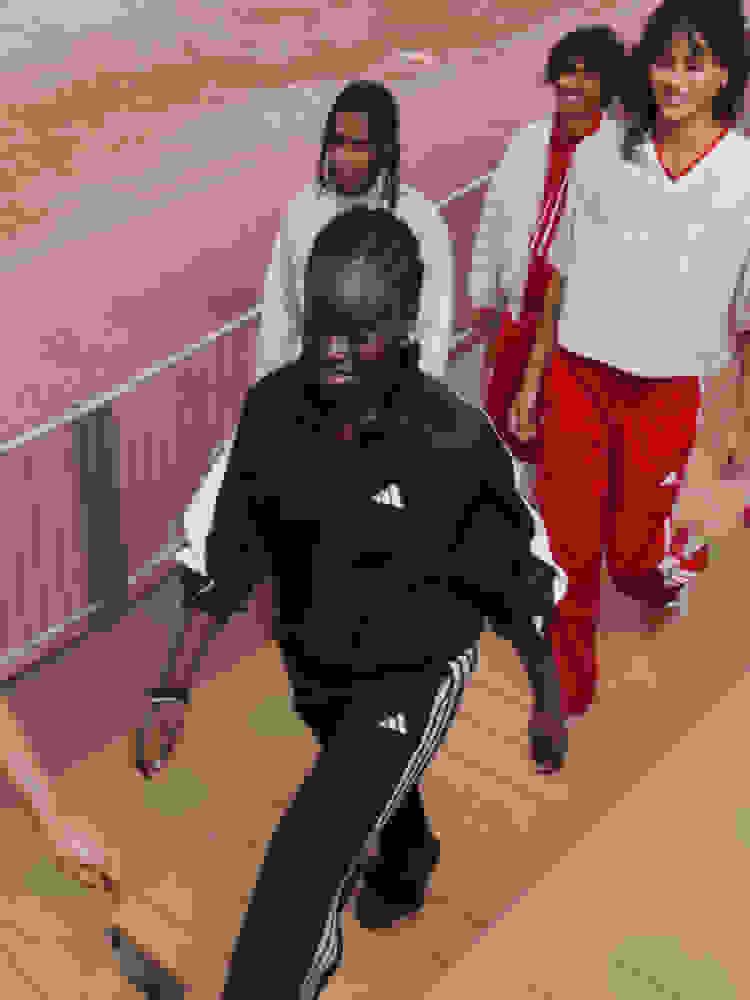 A group of young people, dressed in athletic wear, are walking together on a wooden platform with a red and white background.