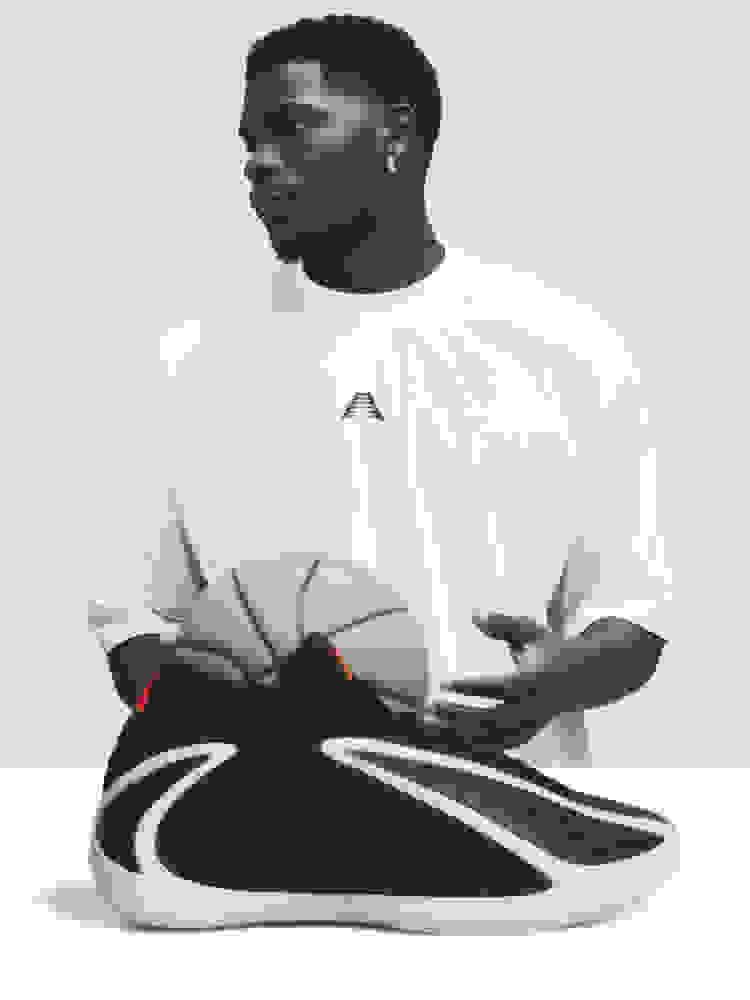 An orange and grey adidas Anthony Edwards 2 basketball sneaker shown angled against a orange background. It has a sculpted sole and wave-like side design. 