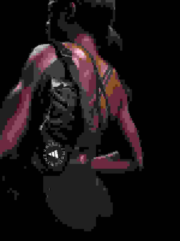 A person wearing a black sports bra and leggings, with a backpack on, stands in a dark setting.