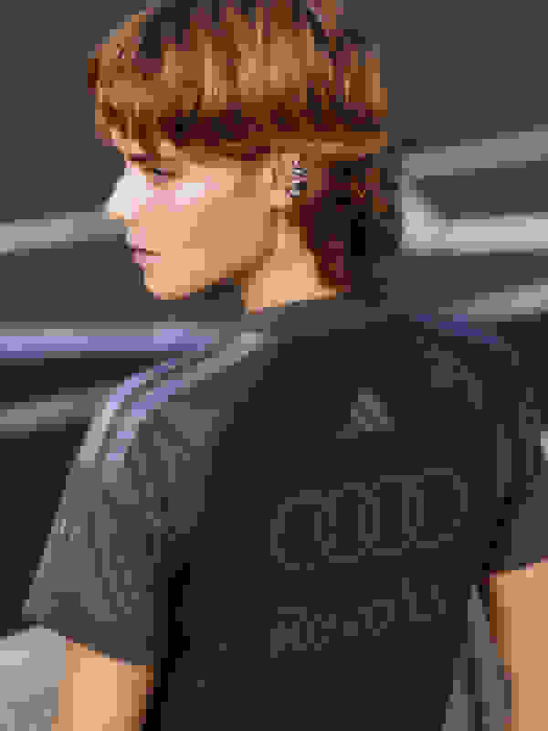 The image shows a person wearing a dark purple Adidas shirt with the Audi logo on the back, standing in front of a dark background.