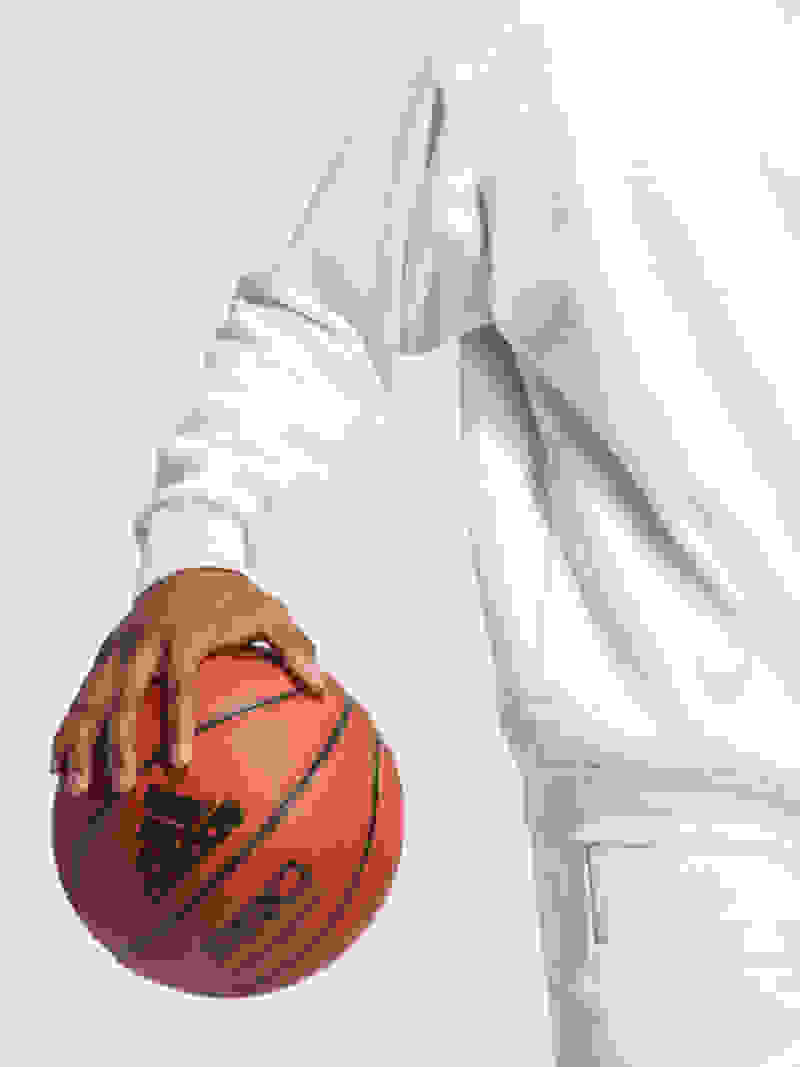 La main d'une personne tenant un ballon de basketball sur un fond blanc uni.