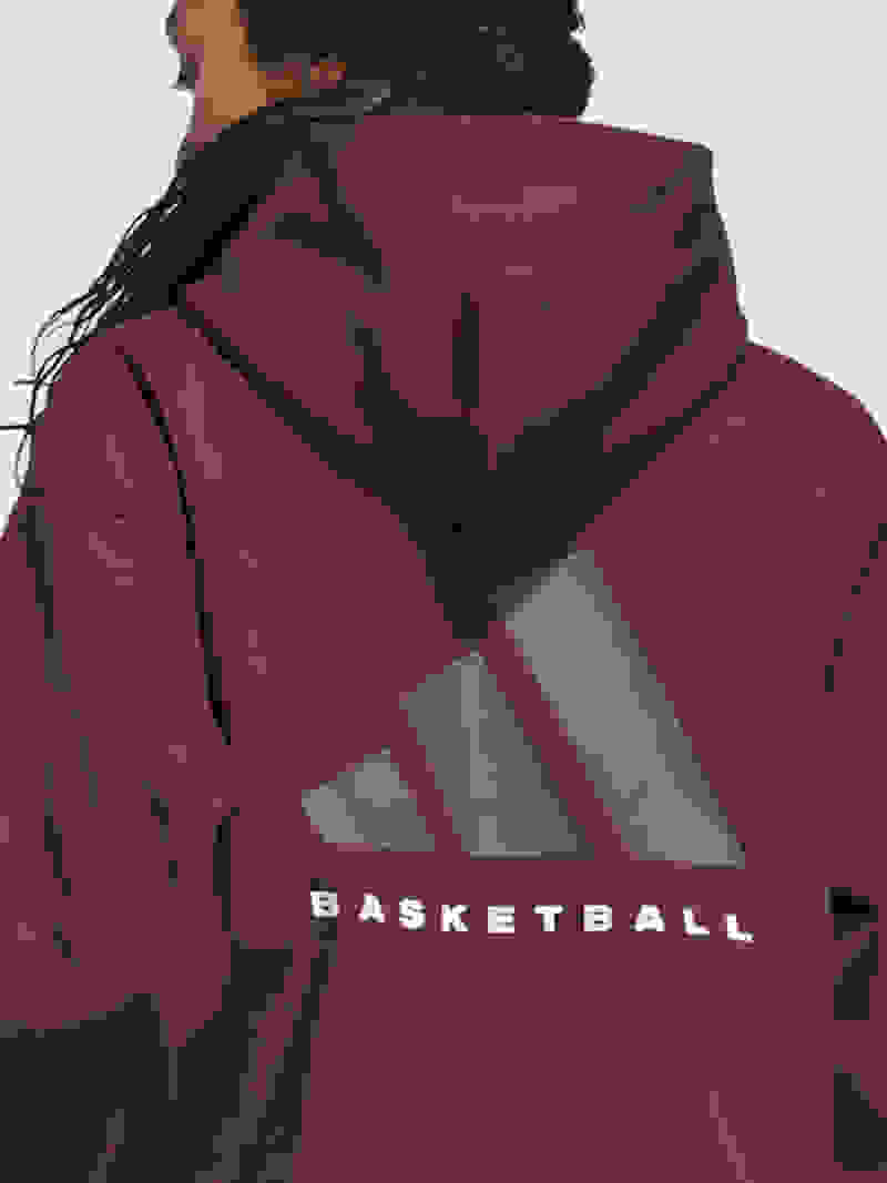A person wearing a burgundy hooded sweatshirt with the word "Basketball" and the Adidas logo printed on the back, standing against a plain white background.