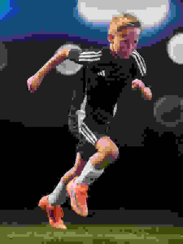 A young soccer player in a black uniform is running on a grassy field with a bright stadium lighting in the background and a pair of the new F50 boots.
