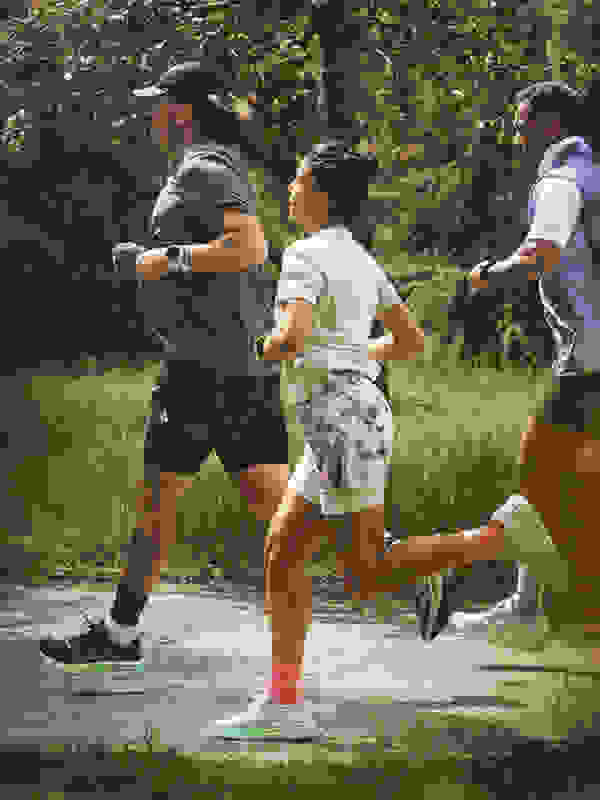 A group of people are jogging together on a dirt path surrounded by lush greenery and trees.