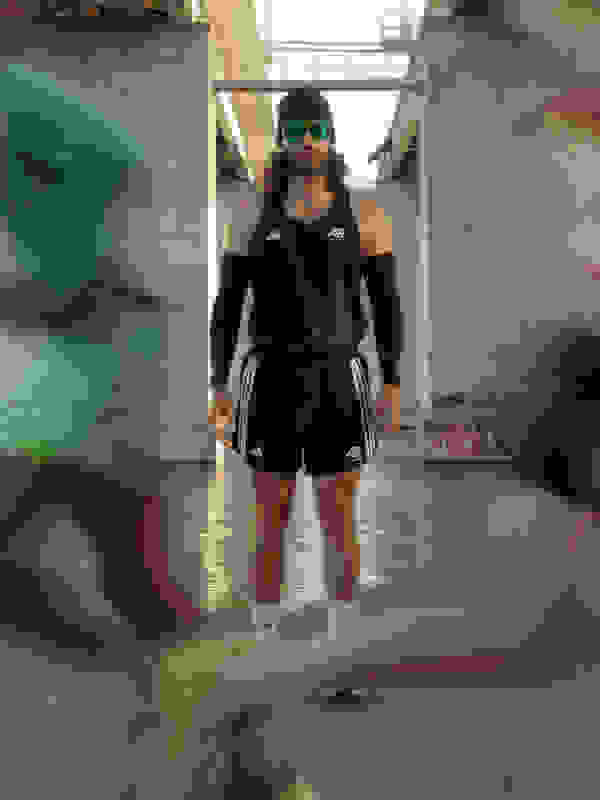 Một người đeo quần áo thể thao và kính mát nổi bật nơi thành thị với những bức tường phủ graffiti ở phía sau.