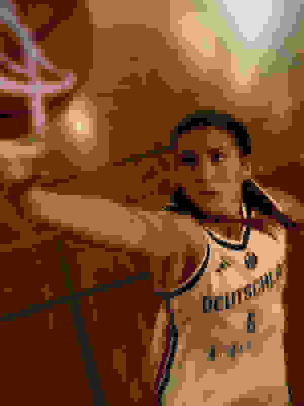 A young woman wearing a white basketball jersey with "Deutschland" printed on it is seen in a basketball court, with a basketball hoop visible in the background.