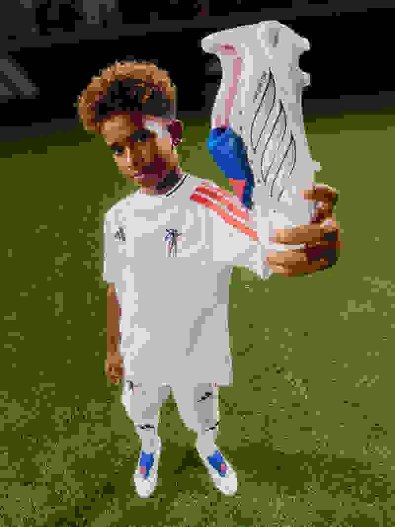 A young boy with curly brown hair poses playfully while showing off the adidas Jude Bellingham kids collection.