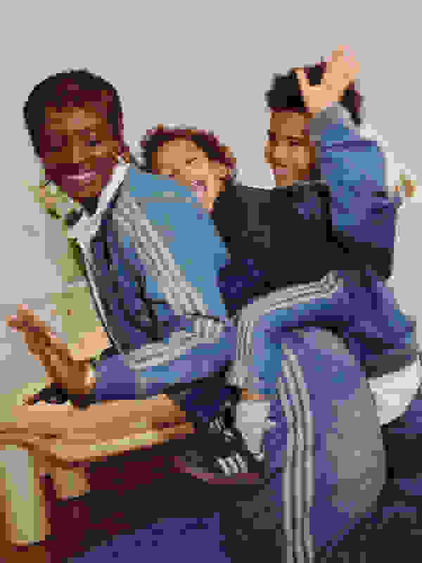 A photo of a mother and her two young sons embracing each other, all wearing variations of denim adidas tracksuits.