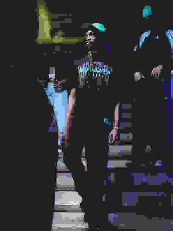 Görüntü, muhtemelen gençlerin sonlarında veya 20'li yaşların başında, loş ışıklı bir ortamda bir dizi merdivende duran bir grup genci gösteriyor. Bireyler, grafik tasarımlı bir tişört de dahil olmak üzere günlük kıyafetler giyiyor ve bir tür sosyal aktivite veya toplanma yapıyor gibi görünüyor.