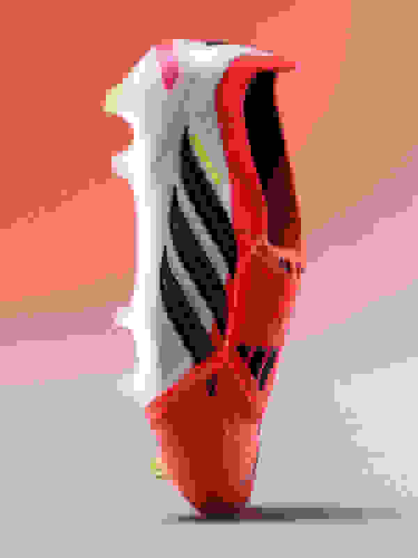 A vibrant, red and white athletic shoe with black and yellow accents, set against a plain coral-colored background.