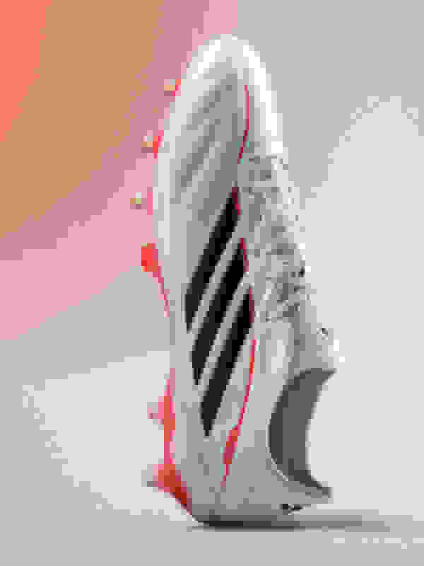 A white and black soccer cleat with red accents, set against a plain pink background.
