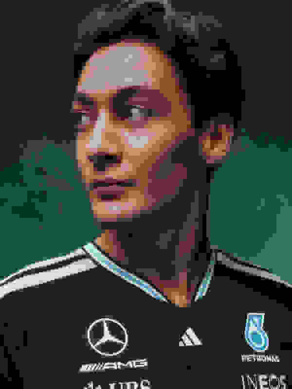 Ein junger Mann mit dunklen Haaren und ernsthaftem Gespür für den Sport, der ein schwarzes Sporttrikot mit weißen und blauen Akzenten trägt, steht vor einem dunkelgrünen Hintergrund.