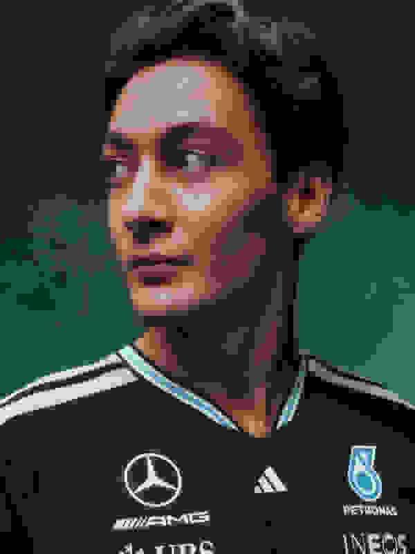 Un jeune homme aux cheveux foncés et à l'expression sérieuse, portant un maillot de sport noir aux détails blancs et bleus, se tient sur un fond vert foncé.