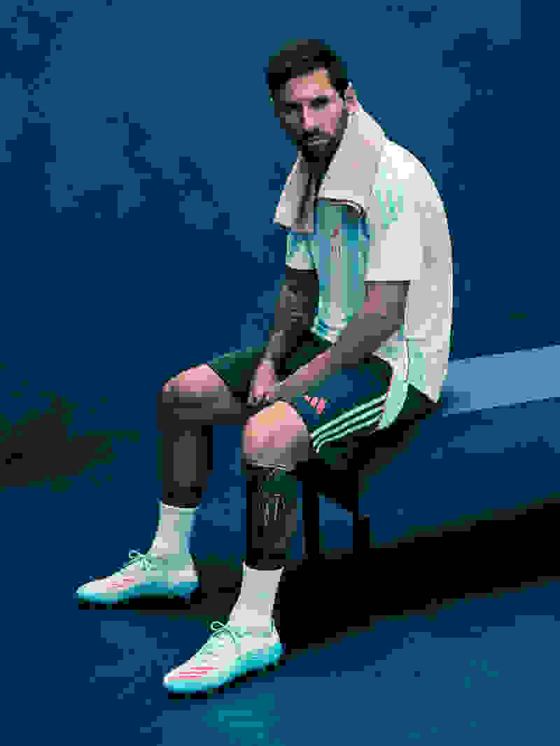 Lionel Messi นั่งอยู่บนม้านั่งในห้องแต่งตัวในสตูดิโอที่มีแสงสีฟ้า พร้อมนำเสนอไอเทมอาดิดาสใหม่ล่าสุดและพร้อมลงสนาม