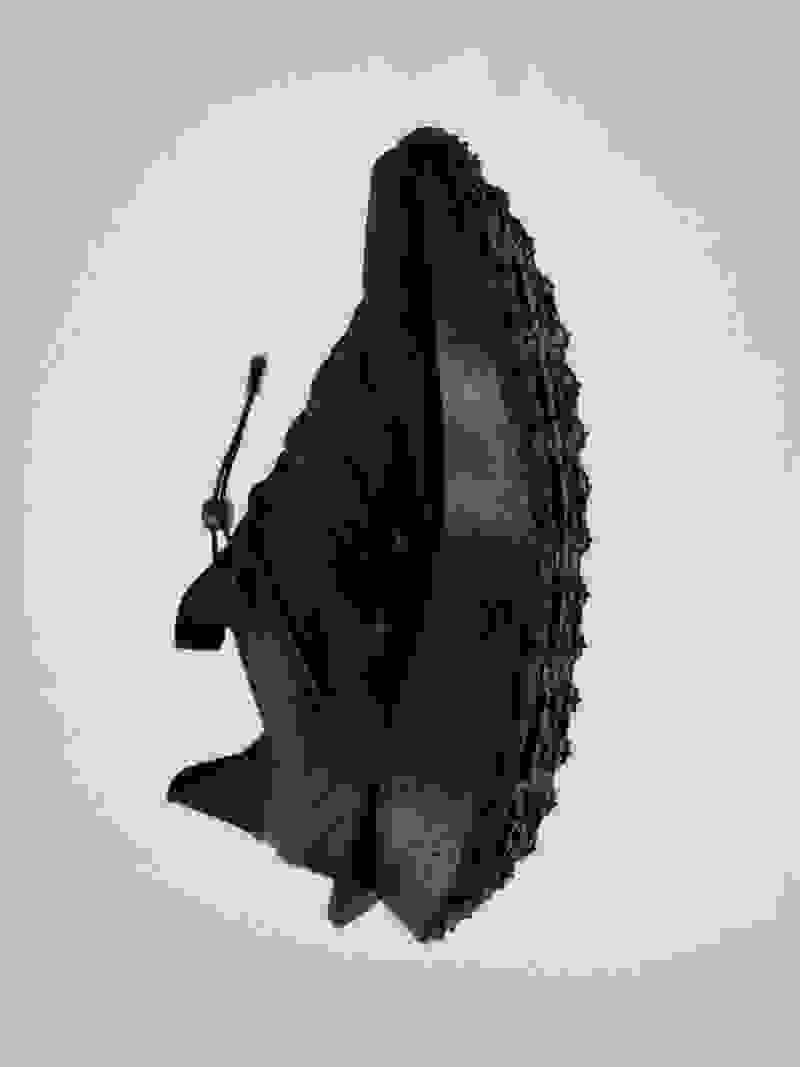 Düz, açık renkli arka planda dokulu yüzeye ve çıkıntılı sapa sahip siyah, sağlam görünümlü bir nesne yer alır.