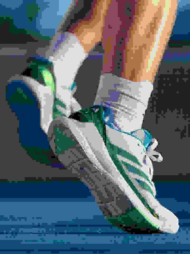 A pair of athletic padel shoes with green and white accents rests on a blue padel court, showcasing the person's active lifestyle.