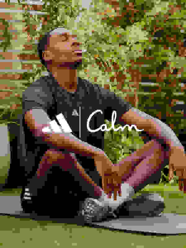 A person wearing a black t-shirt with the word "Calm" printed on it is sitting on a yoga mat in a lush, green outdoor setting.