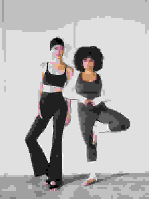 Two women in athletic wear, one with straight black hair and the other with curly dark hair, are posing against a plain white background.
