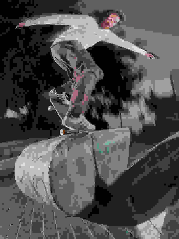 A skateboarder wearing a white long-sleeve shirt, brown pants, and gray adidas Glenburn sneakers performs a trick on a concrete structure.