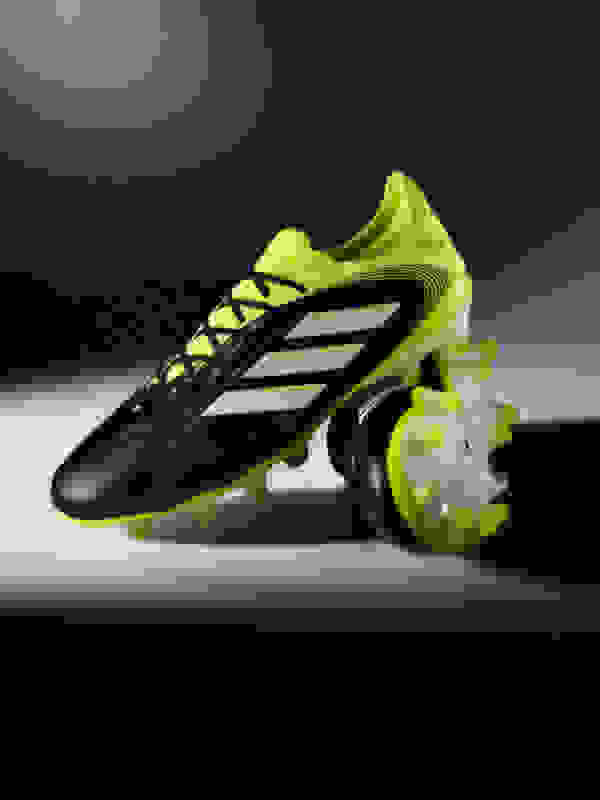 A pair of black and neon green soccer cleats with a dark background.