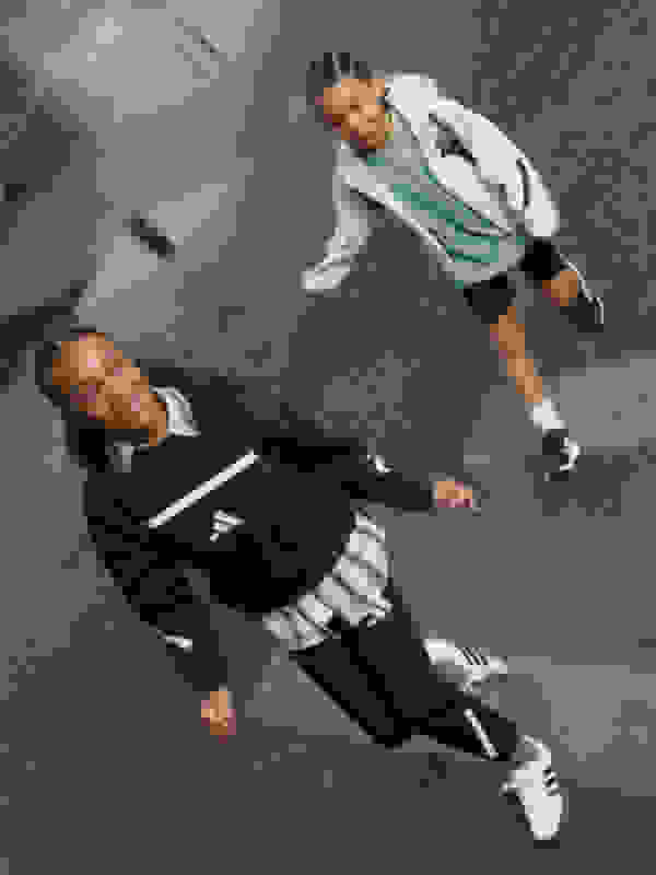 Two young women wearing athletic clothing are standing on a gray floor with a checkered pattern, one appears to be reaching out to the other.