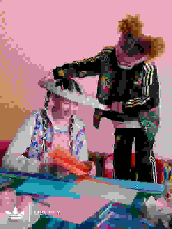 Two sisters are making crafts at the dining room table in adidas x Liberty London. The younger sister is putting a paper crown around her older sister's head.
