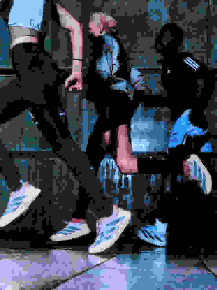 The image depicts a group of people, likely engaged in some form of physical activity or dance, with their legs and feet visible in the foreground against a dark, textured background.