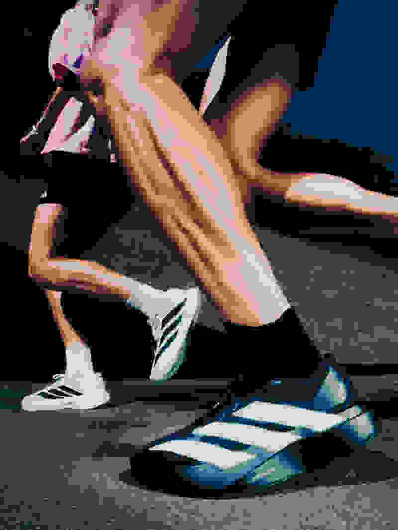The image shows a person's lower body and feet wearing athletic shoes on a dark surface, with a blurred background suggesting an outdoor setting.