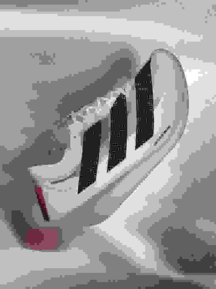 Zdá se, že bílé a černé sportovní boty s červenými detaily se vznášejí na rozmazaném šedém pozadí.