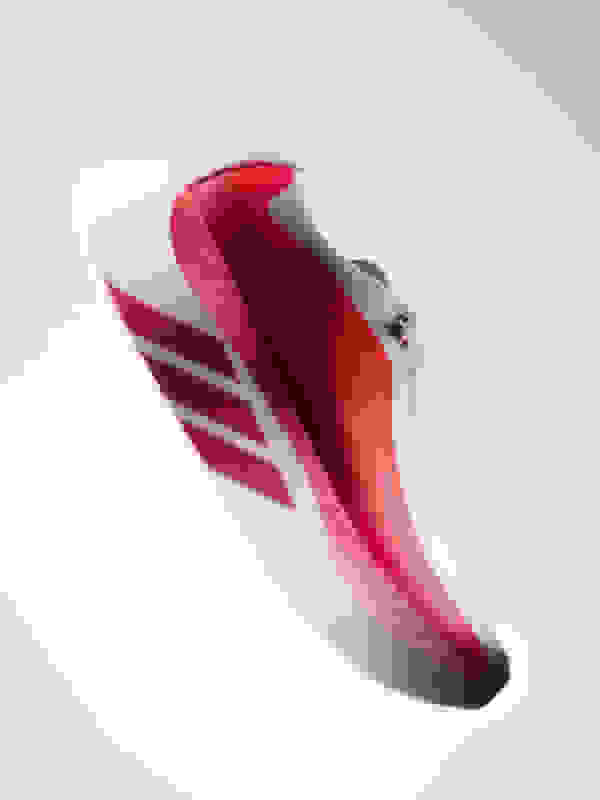 A white and red athletic shoe with distinctive stripes and a sleek, aerodynamic design is the focus of the image, set against a plain white background.