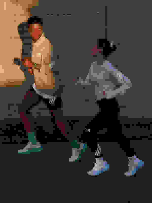 벽돌 벽을 배경으로 희미하게 불이 켜진 거리 위에서 남녀 두 명이 함께 달리고 있다.