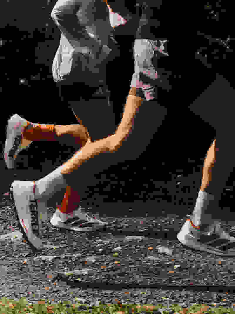 The image shows the lower bodies and legs of two people running on a gravel path at night, with the background appearing to be a wooded area.